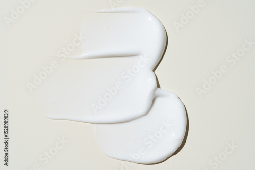 Texture of white cream on beige background. Smear of moisturizer close up. Lotion swatch. Beauty skin care product smear smudge. SPF sunscreen cream sample on pastel background.