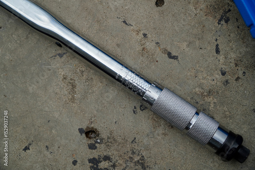 Close-up of a chrome torque wrench resting on a concrete surface.