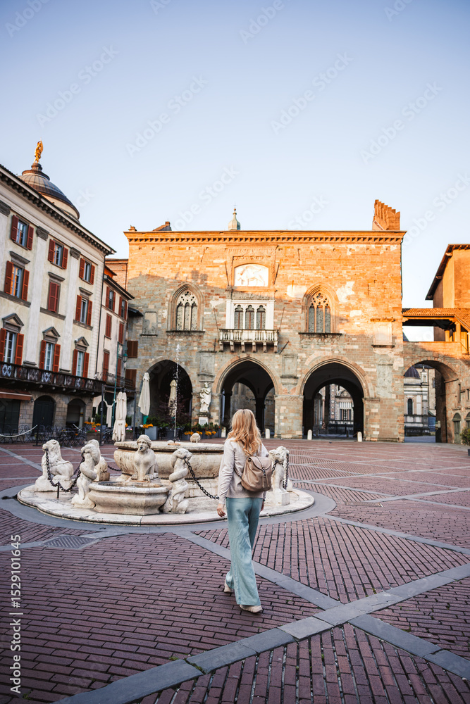 Obraz premium City break on vacation in Italy. Woman tourist walking on town square Piazza Vecchia in Bergamo and exploring famous place. Summer holiday