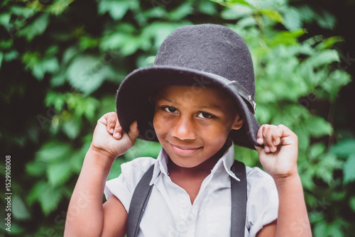 a boy dressed in the style of the 20s pulls his hat down over his ears, holding the brim with both hands