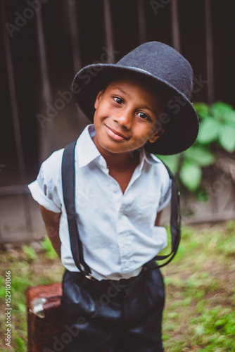 a boy dressed in the style of the 20s with a suitcase on his back looks ingratiatingly at the camera