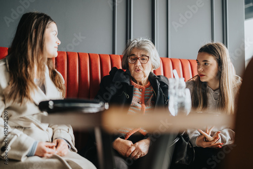 Photos A senior woman sharing a moment with two young women, sitting in a cafe booth