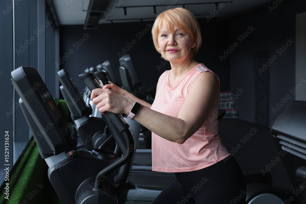 Fototapeta premium Senior woman training on elliptical machine in gym