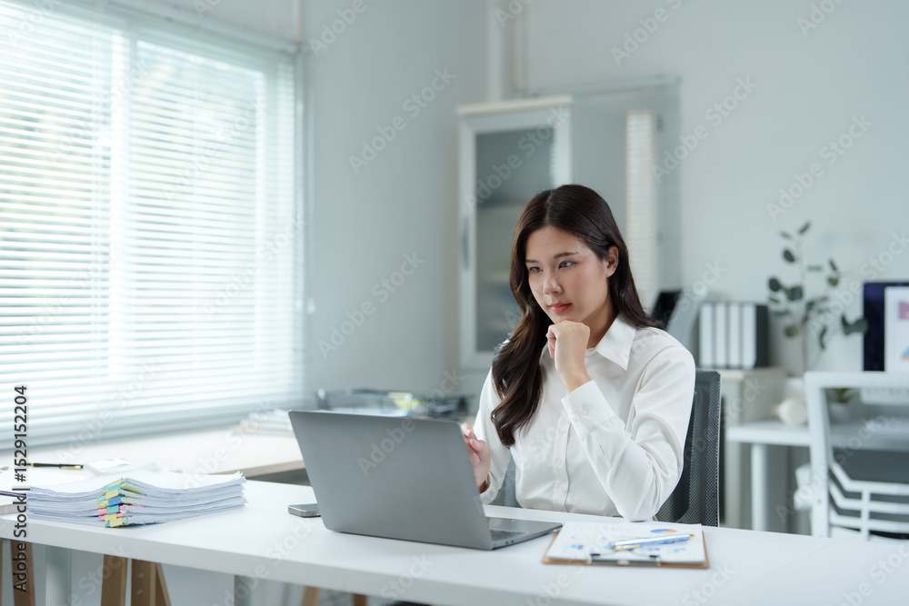 Young professional woman sitting at desk and working using laptop, she is thinking about a new project Young professional woman sitting at desk and working using laptop, she is thinking about a new project