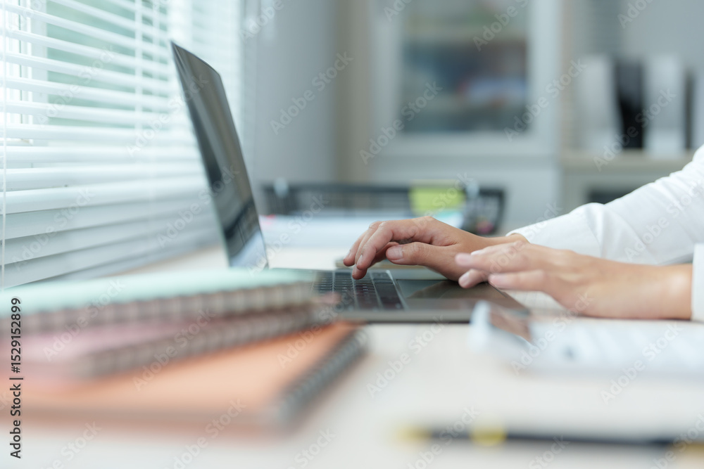 Office worker typing on laptop keyboard near window with blinds Office worker typing on laptop keyboard near window with blinds