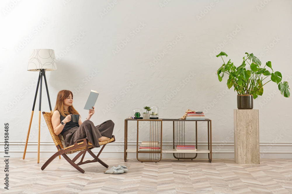 Fototapeta premium A woman is reading a book at home, looking at the phone and tablet. Decorative interior style and vase of plant.