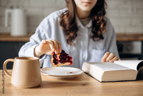 Quadro em tela Close-up of a young woman reading Bible while having breakfast in a kitchen