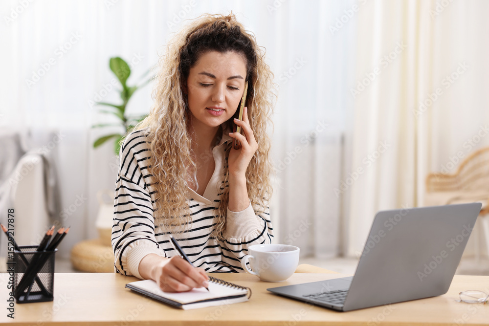 Smiling woman talking by smartphone and working at desk in home office Smiling woman talking by smartphone and working at desk in home office