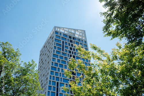 A modern building with a geometric facade, surrounded by green trees, under a clear blue sky. Modern office building with blue sky