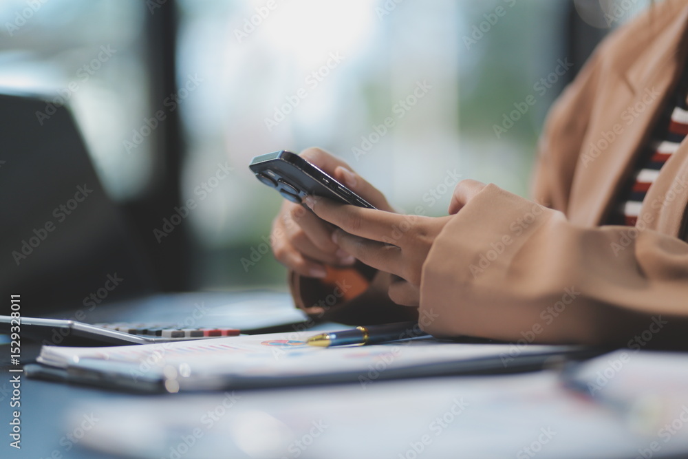Fototapeta premium Young beautiful Asian businesswoman holding smartphone while working in the office room.