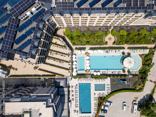 Aerial top-down view of a luxury hotel complex with solar panels, swimming pools, sunbeds, gardens, and a playground. Modern sustainable resort with elegant landscaping and amenities