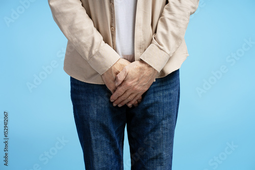 Obraz na płótnie Senior man experiencing discomfort holding groin area on blue background