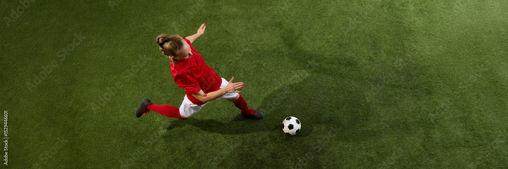 Obraz premium aerial view of female football player stretching to kick ball from above view with dynamic motion on green grassy playground with copy space. Banner. Concept of sport, strength, tournament, energy