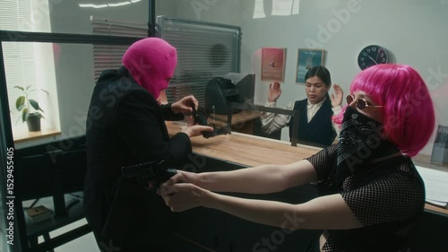 Nervous male robber masked with pink balaclava dropping handgun magazine with clumsy hands threatening teller with weapon while stealing money from bank with female partner