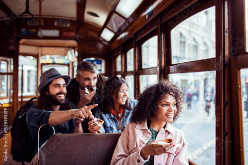 Happy young friends sightseeing on a city tram ride enjoying street food