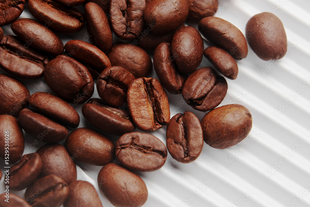 Fototapeta premium Roasted Arabica coffee beans scattered on white ribbed paper of store packaging. Macro. 