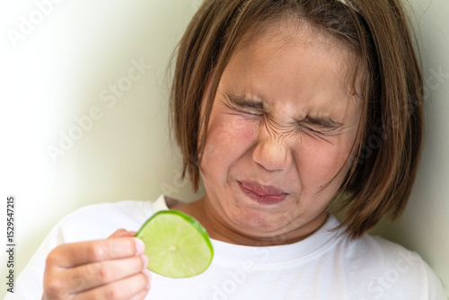 Konstfotografi Eight-year-old girl with short hair grimaces after tasting a sour lime