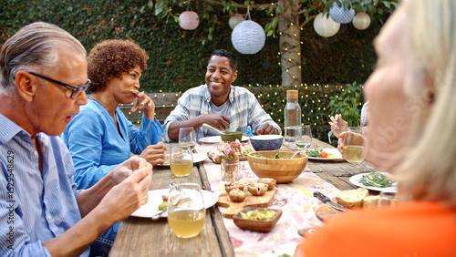 Photos Group Of Mature Friends Sitting Around Table Enjoying Outdoor Meal In Backyard