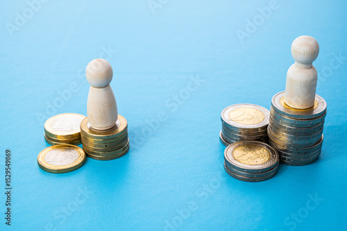 Concept of unequal pay in the workplace between men and women. Wooden figures on piles of coins.