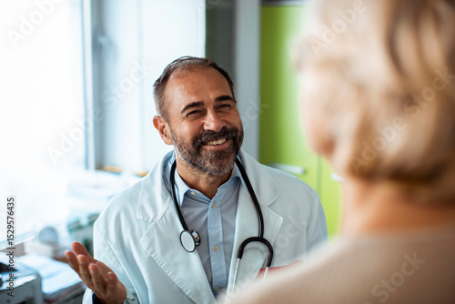Smiling senior doctor talking to female patient during medical consultation in clinic