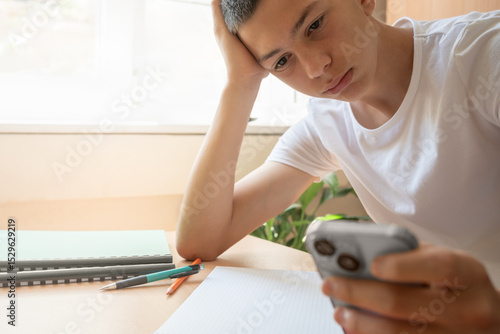 Foto Bored teen boy sitting at table using smartphone