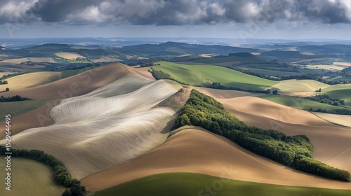 Aerial view rolling farmland, plowed fields, forest, cloudy sky
