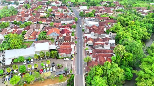 An aerial view reveals a street winding through a town filled with redroofed buildings and lush green trees