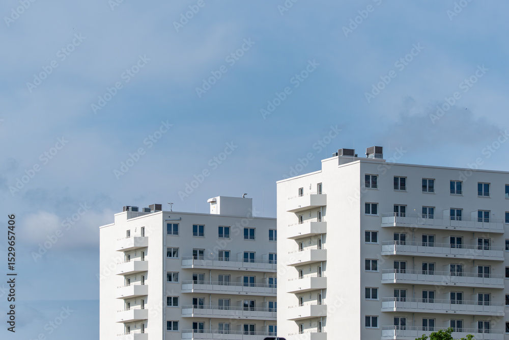Fototapeta premium Modern residential buildings with clean lines and white facades rise into the sky. The sky is slightly cloudy.