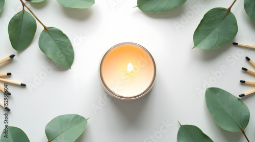 Candle with eucalyptus leaves and matches arranged on a white background