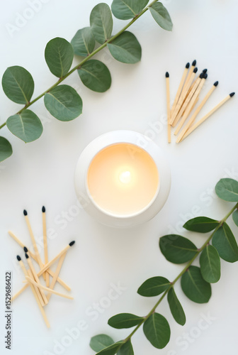 Candle with eucalyptus leaves and matches arranged on a white background