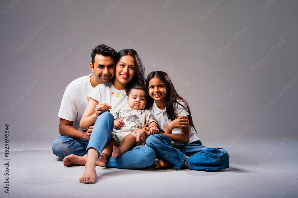 Smiling Indian family looking at camera, sitting together against isolated neutral gray background Smiling Indian family looking at camera, sitting together against isolated neutral gray background