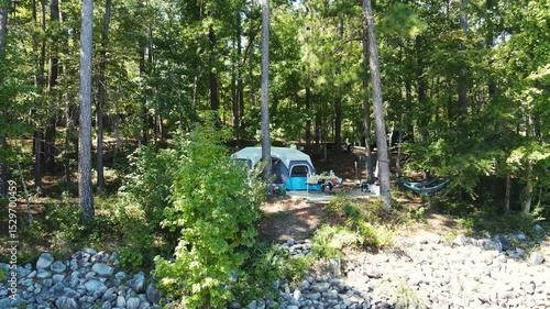 This drone aerial view captures a tranquil summer lake with boats, a sandy beach, and a lush forest, showcasing nature and outdoor scenic beauty ideal for travel and vacation content and a tent.