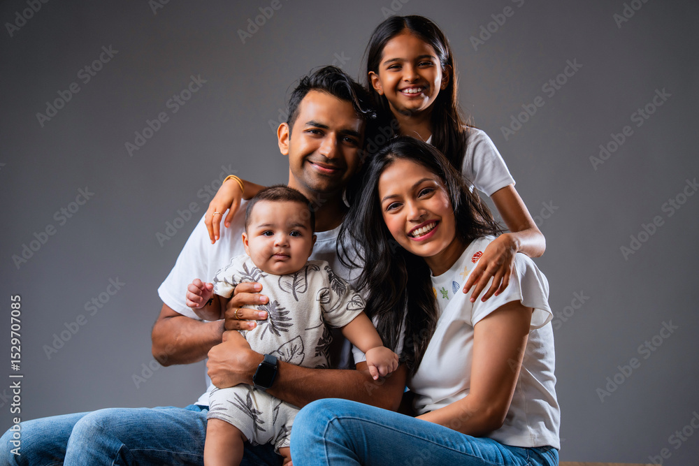 Smiling Indian family looking at camera, sitting together against isolated neutral gray background Smiling Indian family looking at camera, sitting together against isolated neutral gray background