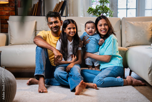 Smiling Indian family sitting on floor near sofa, bonding together in stylish cozy living room