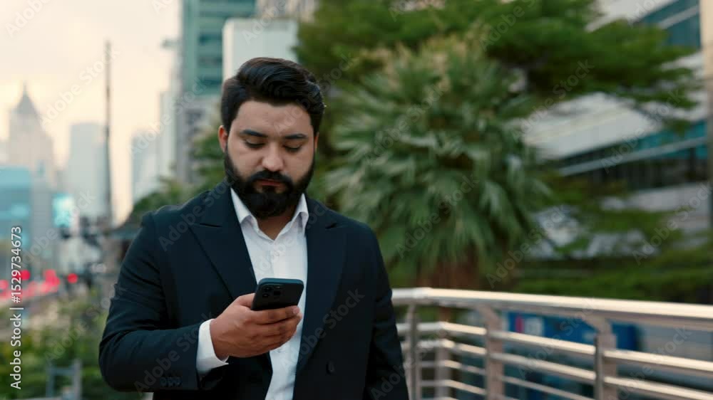 Portrait of serious Indian businessman in formal suit chatting on smartphone on city street. Entrepreneur texts on cell phone walking past office buildings. Business communication Portrait of serious Indian businessman in formal suit chatting on smartphone on city street. Entrepreneur texts on cell phone walking past office buildings. Business communication
