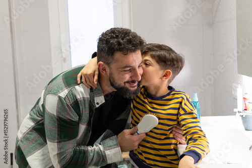 40 years old Father combing his son's hair in the bathroom of their home, son kissing father