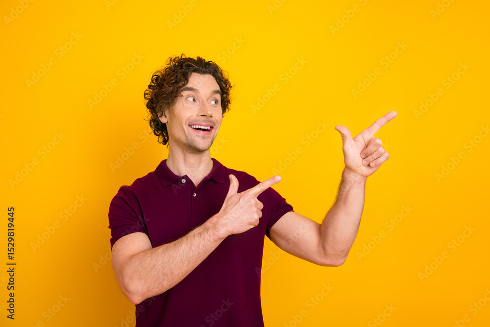 Cheerful young man with curly hair gesturing upwards on a yellow background, wearing a burgundy polo shirt Cheerful young man with curly hair gesturing upwards on a yellow background, wearing a burgundy polo shirt