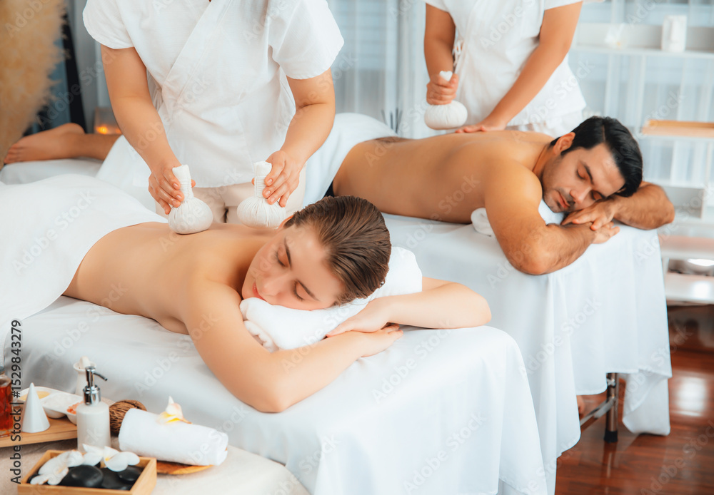 Obraz premium Hot herbal ball spa massage body treatment, masseur gently compresses herb bag on couple customer body. Tranquil and serenity of aromatherapy recreation in day lighting ambient at spa salon. Quiescent
