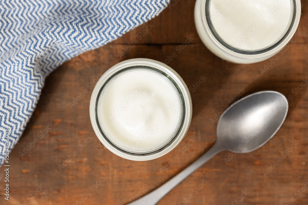 Top view of glass jars of yogurt, wooden table, spoon, and blue cloth. Top view of glass jars of yogurt, wooden table, spoon, and blue cloth.