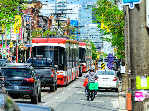 Gig economy: food delivery driver on aan electric bike in busy traffic with cars and light rail street cars shot on a sunny day in Toronto's Queen West district in summer