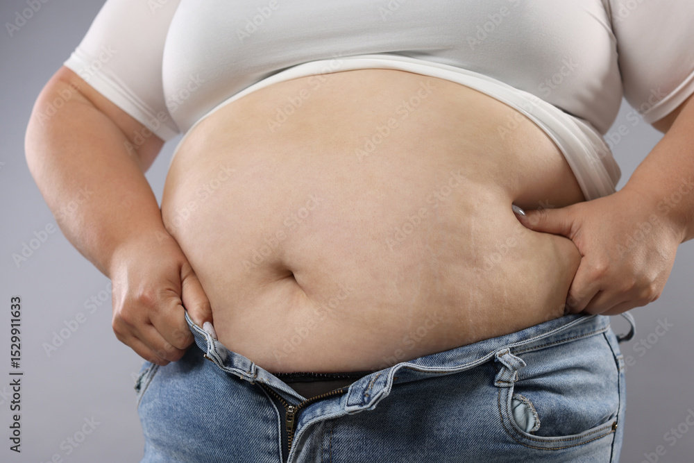 Naklejka premium Woman with excessive belly fat on grey background, closeup. Overweight problem