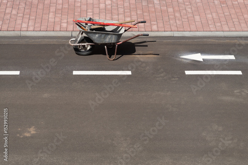 Schubkarre mit Werkzeug auf asphaltierter Strasse mit Radweg