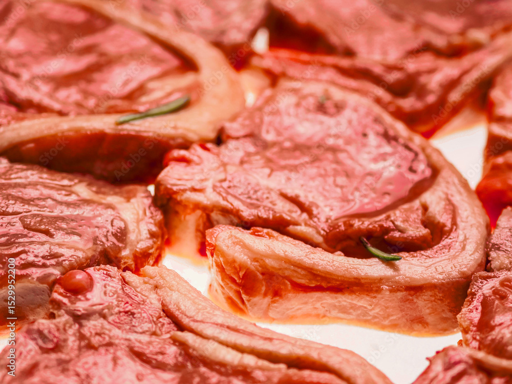 Premium quality marinated lamb loin chops and rosemary herb on white background. Uncooked raw meat on the bone in red color water based marinade to enhance dish taste. Premium quality marinated lamb loin chops and rosemary herb on white background. Uncooked raw meat on the bone in red color water based marinade to enhance dish taste.