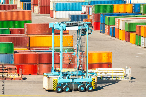 Tableau sur toile Container handler vehicle in cargo terminal with stacked multicolored cargo cont