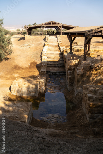 Ancient Baptismal Site: The tranquil scene captures a serene baptismal site, with stone steps leading to a reflecting pool, framed by weathered wooden structures.