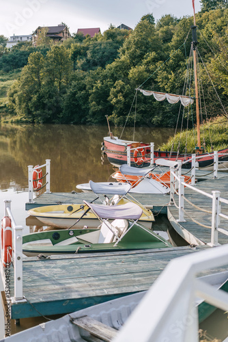 Small riverside dock with pedal boats and vintage wooden sailing skiff in peaceful countryside setting