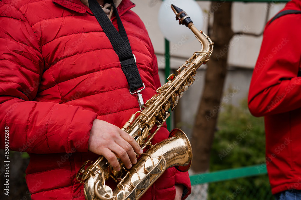 Naklejka premium Saxophone Player in Red Puffer Jacket Performing Outdoors. Brass Instrument, Street Musician, Golden Sax, Music, Urban Scene, Winter Clothing