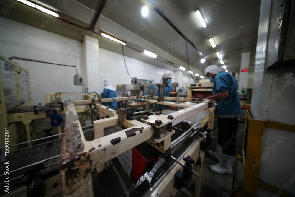 Workers operate machinery in a manufacturing facility during daytime production hours Workers operate machinery in a manufacturing facility during daytime production hours