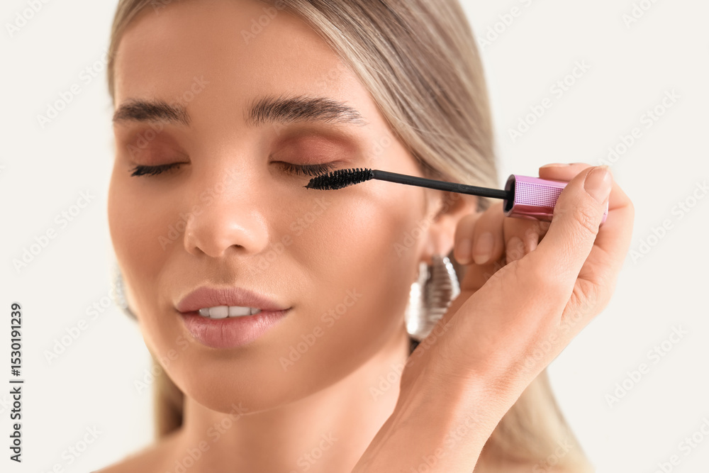 Professional makeup artist applying mascara on young woman in studio, closeup Professional makeup artist applying mascara on young woman in studio, closeup