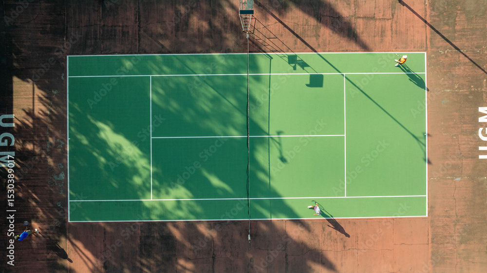 Obraz premium Aerial View of a Tennis Court Game in Progress at UGM, Shadows Dancing on Green Surface